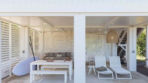 Un espacio al aire libre cubierto con una mesa blanca y bancos, un sofá y sillones de descanso.