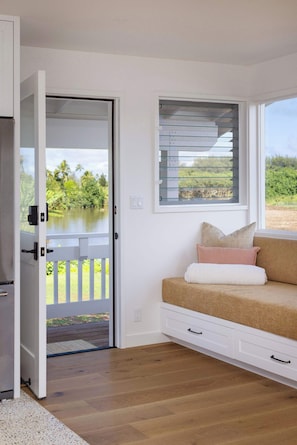 Ein Zimmer mit einer Schiebetür, die auf einen Balkon führt, einem Fenster mit Jalousien, einer Couch mit Kissen und einer weißen Sitzbank.