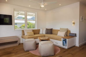 Ein modernes Wohnzimmer mit einer Couch, Hocker, einem Couchtisch, einem Flachbildfernseher und einem Fenster mit Blick.