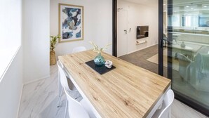 Een moderne eetruimte met een houten tafel, witte stoelen, een vaas met bloemen en een schilderij aan de muur.