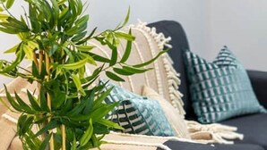 Een woonkamer met een zwarte bank, blauw-witte kussens, een zwarte metalen plantenstandaard en een beige plaid.