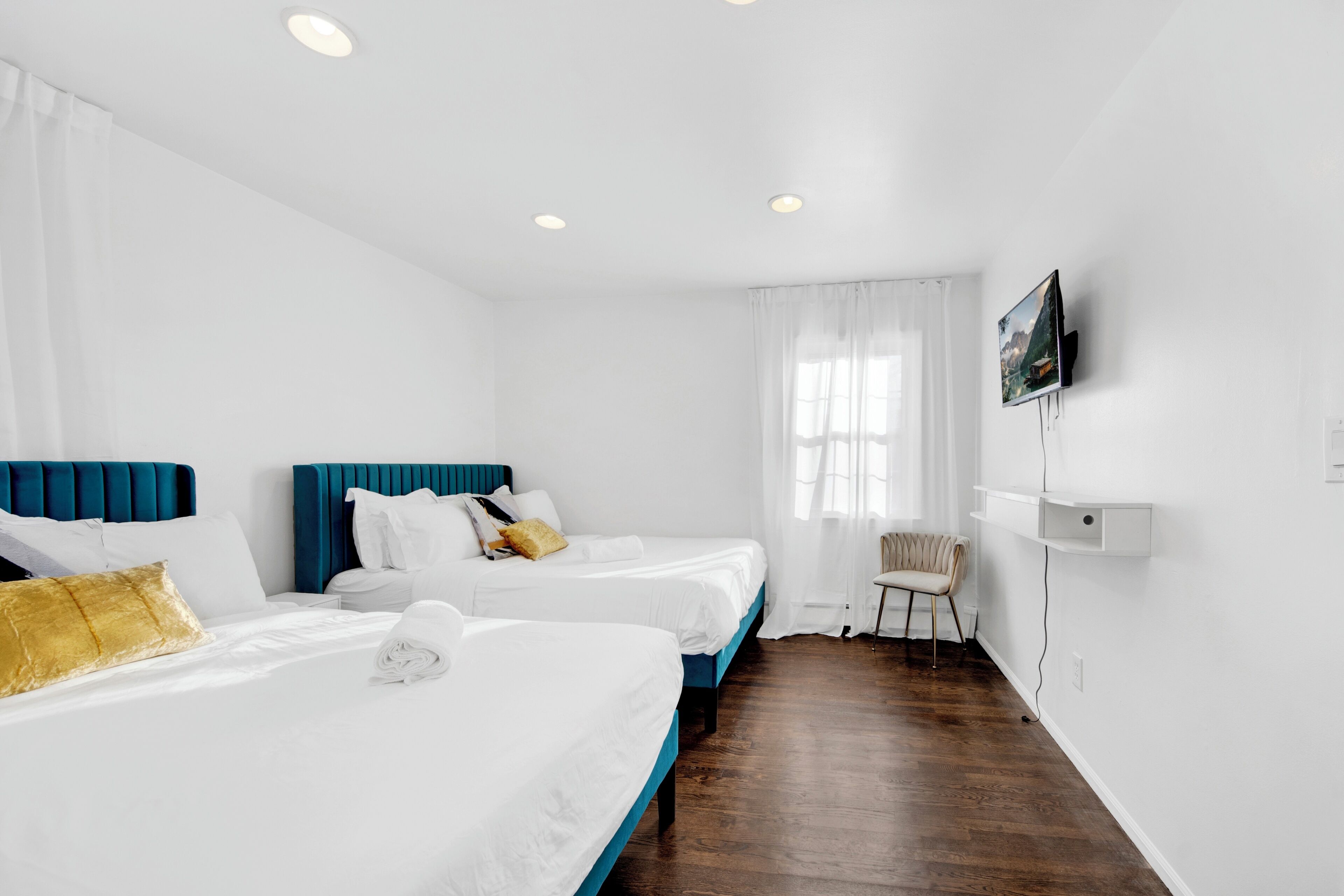 Une chambre d’hôtel avec deux lits, une télévision, une chaise et une fenêtre avec des rideaux.
