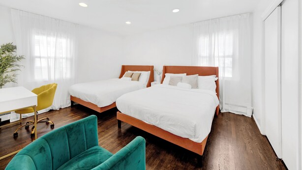 Ein Hotelzimmer mit zwei Betten, einem Schreibtisch, einem Sessel und einer Zimmerpflanze.