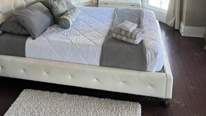 Ein Schlafzimmer mit einem großen Bett, zwei mit Vorhängen versehenen Fenstern, einer Kopfteil und einer kleinen Bank.