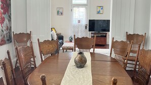 Ein Esszimmer mit einem runden Holztisch, sechs Stühlen, einer Chandelüster und einem Fernseher im Hintergrund.