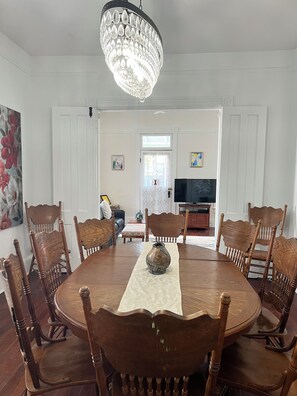 A dining room with a round wooden table, six chairs, a chandelier, and a television in the background. -  Come enjoy Liberty Manor our beautiful Victorian home in downtown St Augustine. (St. Augustine)