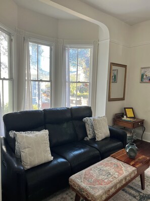 A living room with a black leather sofa, a wooden coffee table, and a patterned ottoman. -  Come enjoy Liberty Manor our beautiful Victorian home in downtown St Augustine. (St. Augustine)