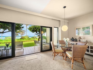 Una habitación moderna con puerta de vidrio a un patio, mobiliario de mimbre, una mesa redonda de vidrio y una lámpara colgante.
