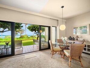 A modern room with a glass door leading to a patio, wicker furniture, a round glass table, and a pendant light.