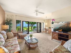 A spacious living room with a large TV, comfortable seating, a ceiling fan, and a view of the outdoors.