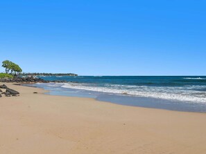 A beach with clear skies, calm waves, and a distant shoreline with buildings.