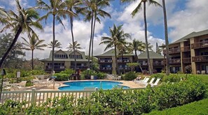 A hotel with a pool, palm trees, and a clear sky.