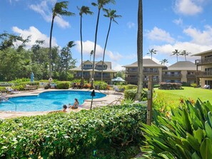 A resort with a swimming pool, palm trees, and a well-maintained lawn.