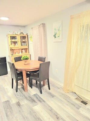 A dining area with a wooden table, four chairs, a cabinet with dishes, and a window with curtains.