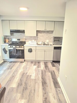 A modern kitchen with white cabinets, a stainless steel stove, a dishwasher, and a microwave.
