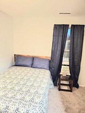 A bedroom with a bed, a small table, and a window with curtains.