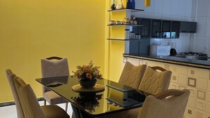 Een moderne keuken met een gele accentmuur, een eettafel met stoelen en een keukentrap aanrecht met apparatuur.