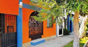 A building with a bright orange facade, a black wrought iron gate, and a tree-lined pathway. - CASITA VERSALES PRIME LOCATION IN PUERTO VALLARTA (Puerto Vallarta)