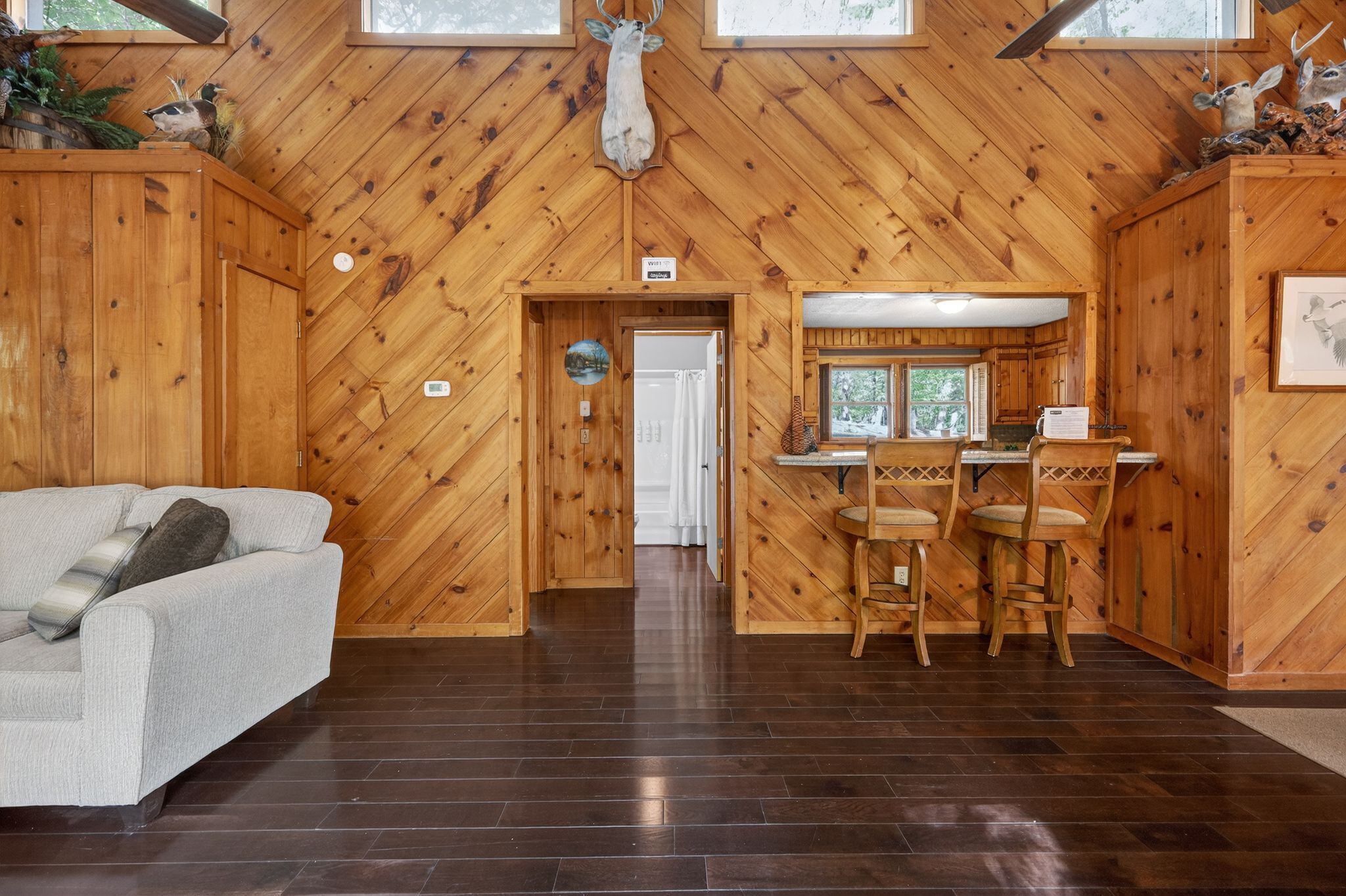 Un intérieur en bois avec un canapé, un coin repas avec des chaises et une porte donnant sur une autre pièce.
