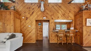 A wooden interior with a sofa, a dining area with chairs, and a door leading to another room. - Moneta Memories Lake Retreat | Hot Tub & Fire Pit (Moneta)