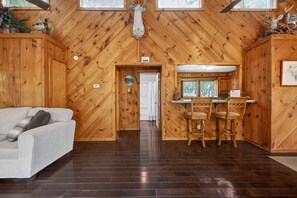Un intérieur en bois avec un canapé, un coin repas avec des chaises et une porte donnant sur une autre piÚce.