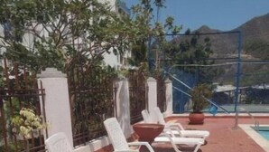 Une terrasse sur le toit, avec des chaises longues blanches, des plantes en pot et une piscine en arrière-plan.