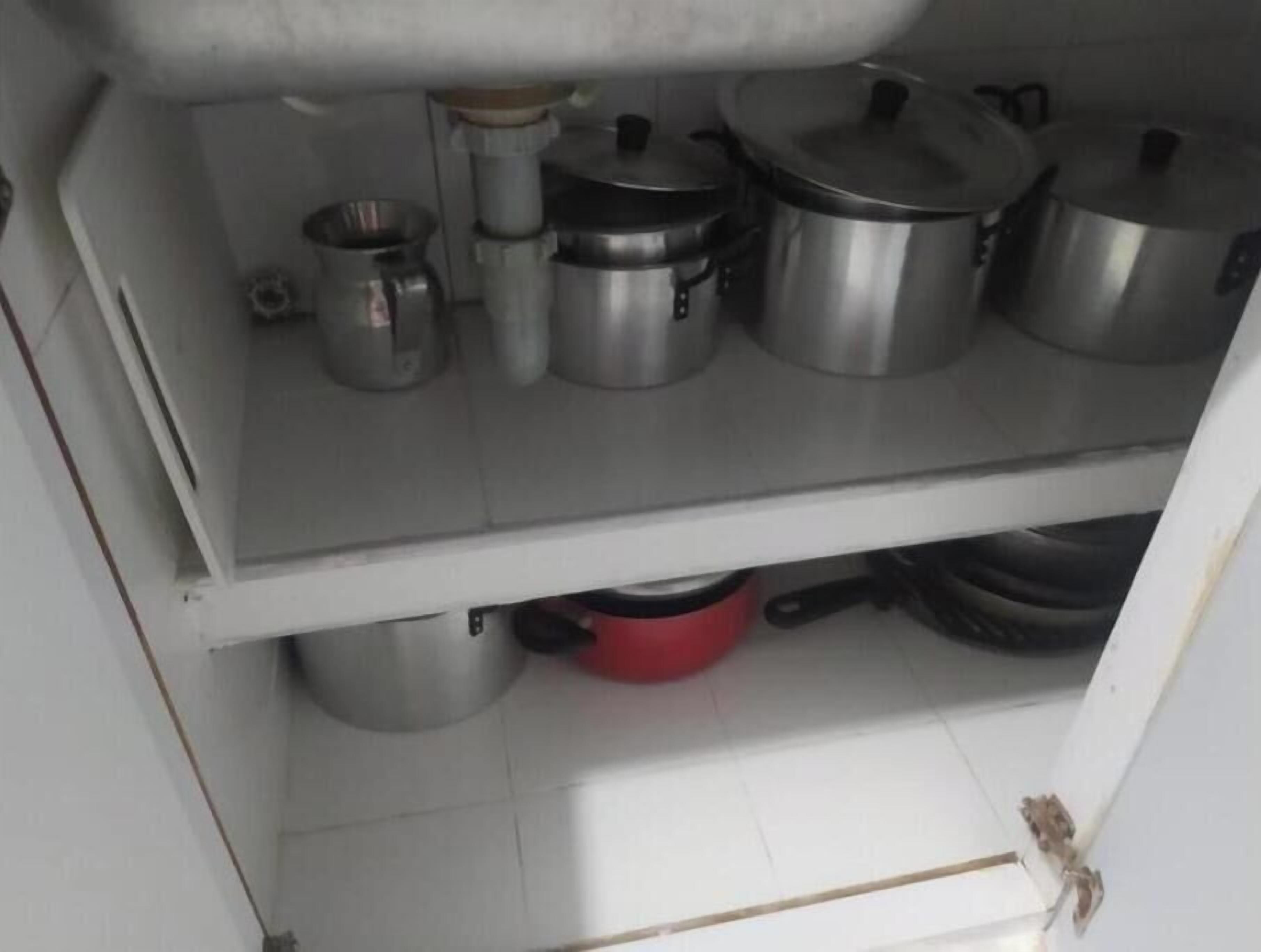 Una cocina con ollas y sartenes de acero inoxidable en estantes, una olla roja en el estante inferior y un suelo de baldosas blancas.