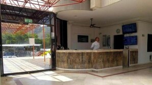 Un espace d’accueil doté d’un sol en marbre, d’un comptoir de réception, d’un ventilateur de plafond et d’un téléviseur fixé au mur.