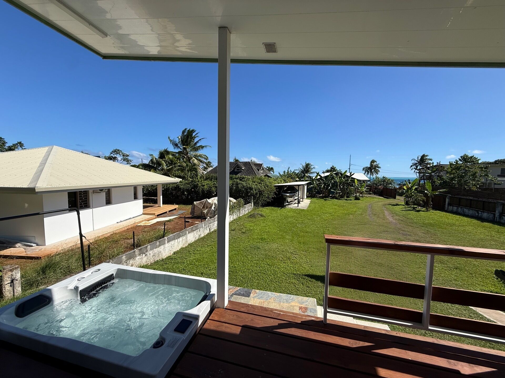 A hot tub on a wooden deck with a view of a grassy yard and a house.