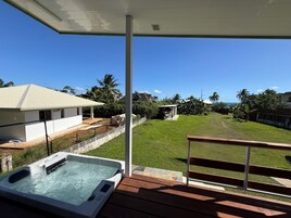 Un jacuzzi en una terraza de madera con vista a un jardín césped y una casa.