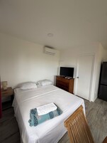 A hotel room with a bed, a TV on a wooden dresser, a white door, and a refrigerator.