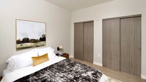 A bedroom with a bed, a nightstand, a lamp, a painting, and two wardrobes. - Walker`s Point Apt with Gym and Balcony | Sleeps 4-5 (Milwaukee)