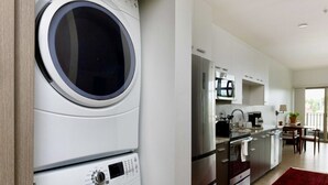 A compact kitchen with built-in appliances, a dining area with a red rug, and a laundry room with stacked washers and dryers. - Walker`s Point Apt with Gym and Balcony | Sleeps 4-5 (Milwaukee)