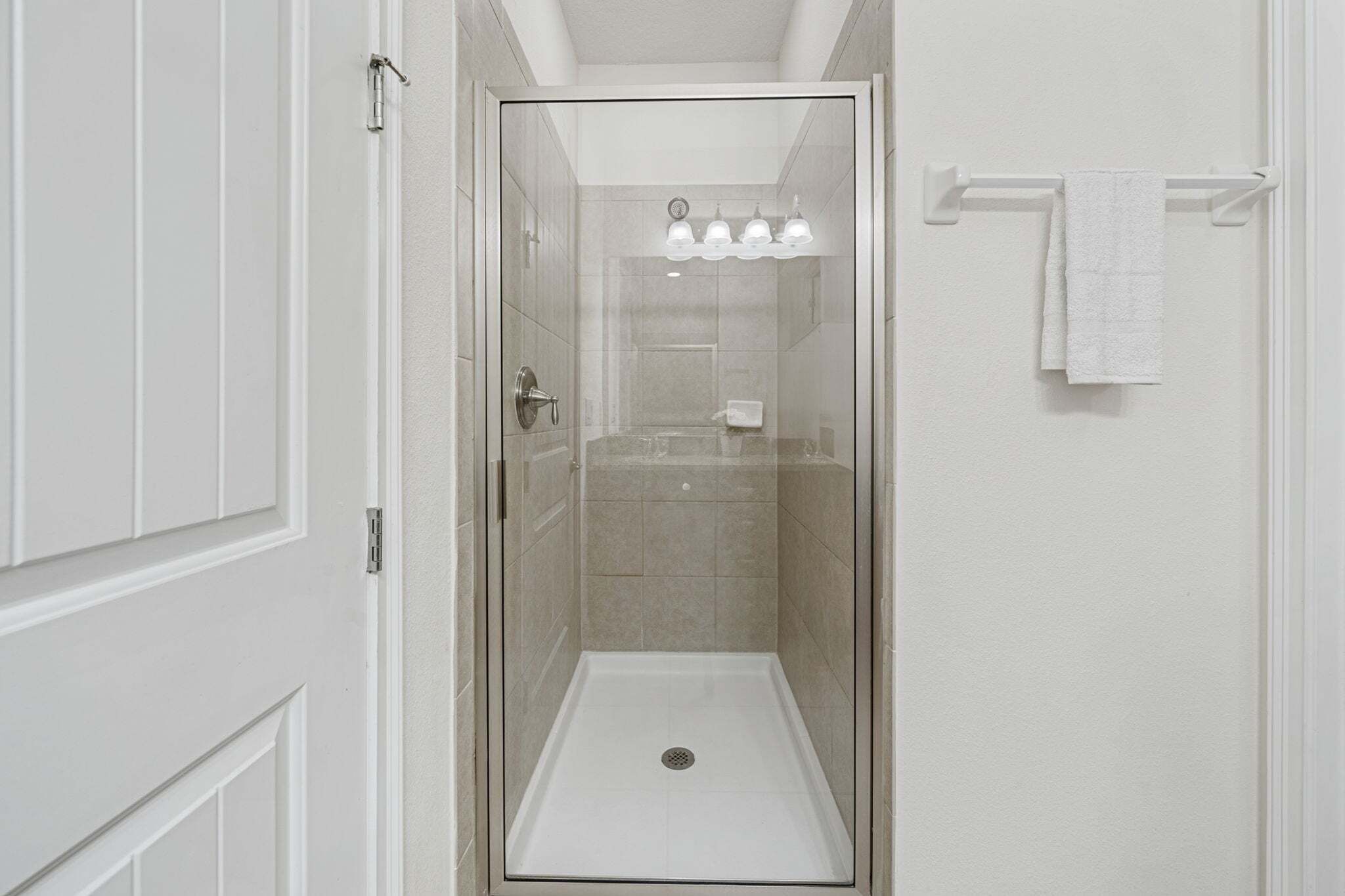 A glass-enclosed shower stall with a white towel rack and a light fixture above the shower.