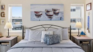 Een slaapkamer met een bed, twee nachtkastjes, een raam en een schilderij van boten.