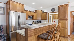 A kitchen with wooden cabinets, a stainless steel refrigerator, a microwave, and a coffee maker. - 46mm Lakefront Home w/ Private Dock, Great Views, Huge Deck & Water Toys (Gravois Mills)