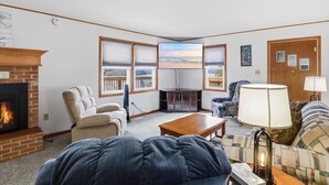 A living room with a fireplace, a television, and a view of the ocean through large windows. - 46mm Lakefront Home w/ Private Dock, Great Views, Huge Deck & Water Toys (Gravois Mills)