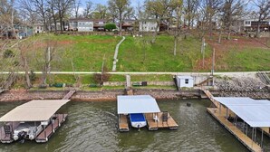 A waterfront dock with boats, a small dockside building, and a grassy area with trees. - 46mm Lakefront Home w/ Private Dock, Great Views, Huge Deck & Water Toys (Gravois Mills)