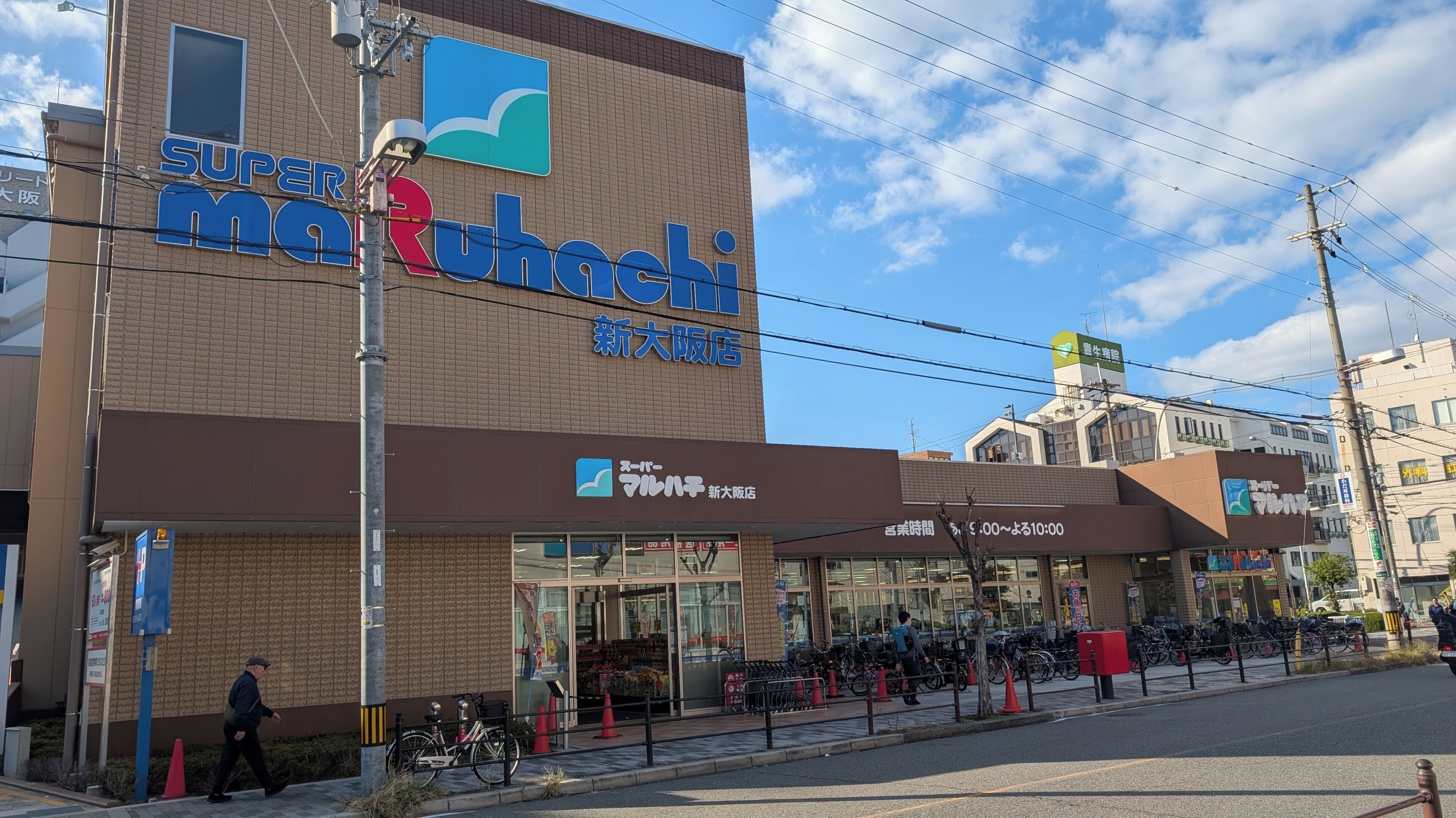Una tienda Supermarket Marunomi con entrada despejada, zona de estacionamiento visible y espacio para bicicletas.