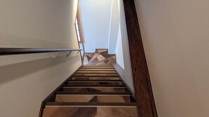 Eine Treppe mit Holzbodenstufen und einer Metallgeländer, die zu einer Zwischenebene mit einer Wand im geometrischen Muster führt.