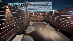 Eine Dachterrasse mit Holzgeländern, einer ebenen Fläche und Blick auf ein Gebäude im Hintergrund.