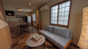 Ein Wohnzimmer mit einer Couch, einem Esstisch mit Stühlen, einer Küchenzeile und großen Fenstern.