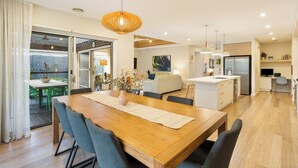 Una cocina moderna con una isla central, un comedor con mesa y sillas de madera, y una sala de estar con sofá y televisor.