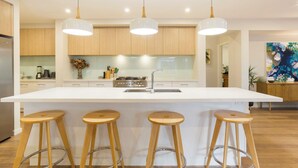 Una cocina moderna con una isla central, taburetes de madera, luces colgantes y una estufa de acero inoxidable.