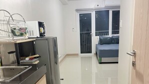 Una cuina moderna amb nevera, microones i rentapelats. Es veu, al fons, una zona de menjador amb sofà i un balcó.