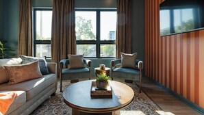 Een moderne woonkamer met een bank, twee fauteuils, een salontafel en een groot raam met gordijnen.