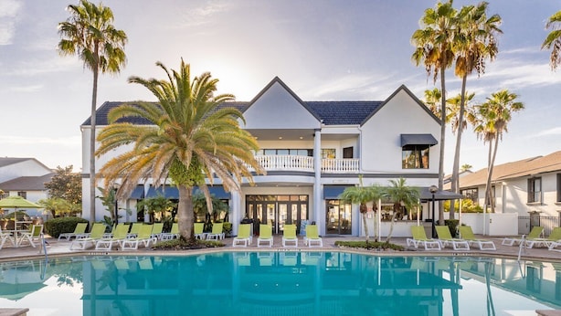 A pool with lounge chairs, palm trees, and a building with a balcony. - Legacy Vacation Club Resort 3 BR 2 BA Condo (Kissimmee)