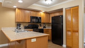 A kitchen with wooden cabinets, a black refrigerator, a microwave, and a sink. - Legacy Vacation Club Resort 3 BR 2 BA Condo (Kissimmee)