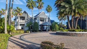 A large, two-story building with a stone facade and a balcony, surrounded by palm trees and a paved driveway. - Legacy Vacation Club Resort 3 BR 2 BA Condo (Kissimmee)