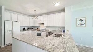 A modern kitchen with white cabinets, a granite countertop, stainless steel appliances, and a pendant light. - Beautiful 7BR Beach House, Pool, Walk to Beach (North Myrtle Beach)